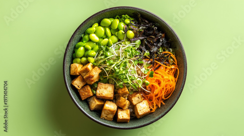 A healthy bowl filled with tofu, edamame, shredded carrots, sprouts, and seaweed