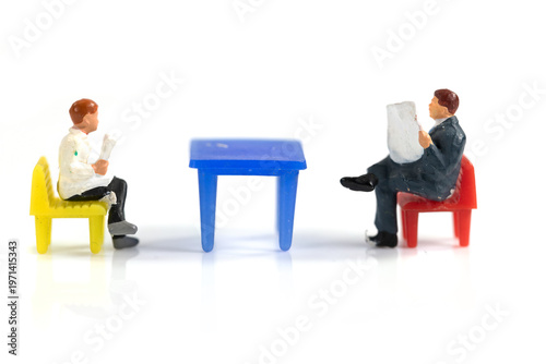 Miniature Business Meeting With Two Figurines Sitting at Colorful Table Reading Documents and Discussing Ideas
