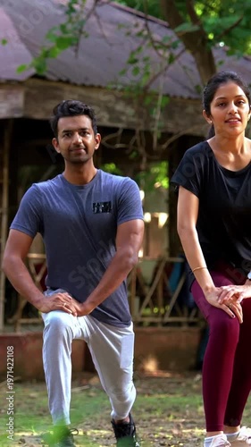 Young Indian couple stretching legs standing outdoors after exercising together in green city park