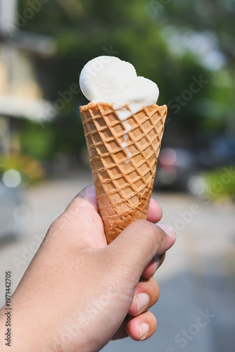 A hand holding a vanilla ice cream cone.