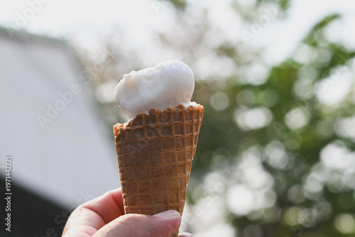 A hand holding a vanilla ice cream cone.