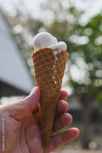 A hand holding a vanilla ice cream cone.