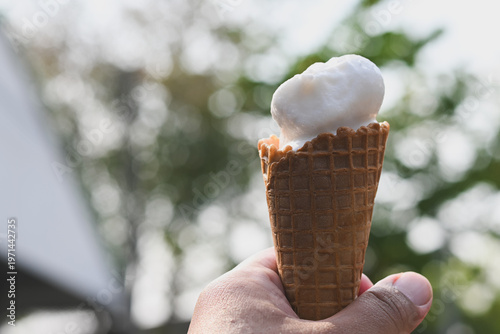 A hand holding a vanilla ice cream cone.