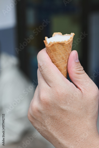 A hand holding a vanilla ice cream cone.