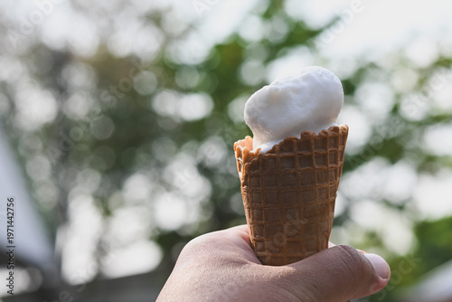 A hand holding a vanilla ice cream cone.