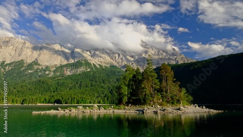 Video shot of a pine-covered island in Eibsee lake with the towering Zugspitze mountain range and clouds in the Bavarian Alps, Germany.