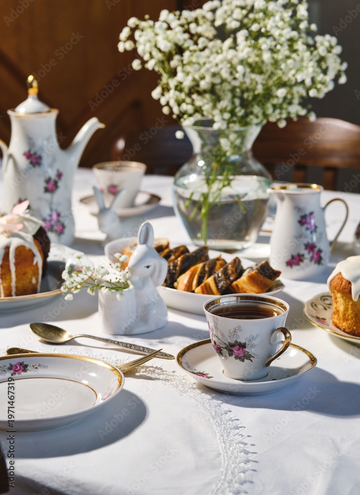 Fototapeta premium A spring Easter table setting with a vintage coffee set, Easter cupcakes, and a poppy seed roll on a white tablecloth. Happy Easter.