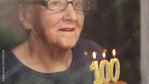 Portrait of an elderly woman with glasses holding anniversary candles.  An old woman holds a birthday cake alone on her centenary.