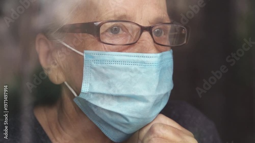 Portrait of an elderly woman in a window after quarantine with her mask removed. An old woman in a window with her mask down, after the pandemic.