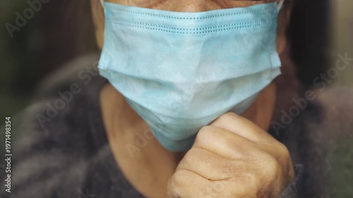 Portrait of an elderly woman in a window after quarantine with her mask removed. An old woman in a window with her mask down, after the pandemic.