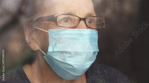 Portrait of an elderly woman in a window after quarantine with her mask removed. An old woman in a window with her mask down, after the pandemic.
