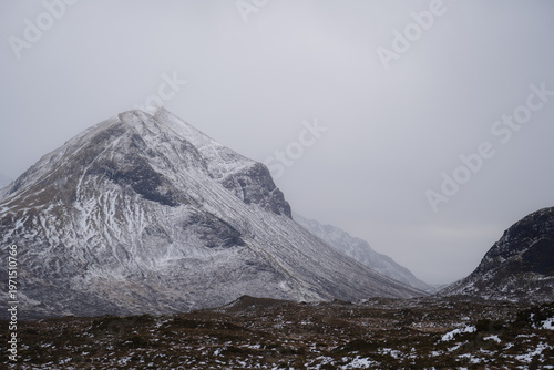 View of snow-dusted peaks rise majestically against a misty sky, casting long shadows across the rugged terrain, Sligachan, Isle of Skye, Scotland.