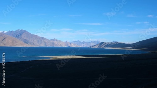 Cinematic shot of Pangong Lake during early morning, with soft golden light reflecting on the calm water as birds gently glide across the surface. Ideal moment for travel and nature storytelling.