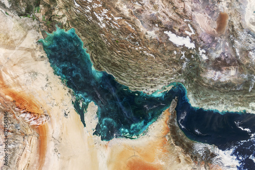 Satellite view of the Persian Gulf showcasing turquoise waters, swirling plankton blooms, and the rugged desert coastlines of the Middle East. High-contrast aerial photography of Earth.