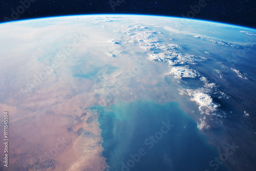 Stunning cinematic view of Earth from space, showing the planet's curvature, thin blue atmosphere, and swirling white clouds over vast desert terrain and deep blue oceans under a starry sky.