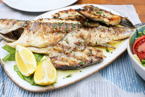 Grilled fish served on plate with lemon and herbs. Delicious seafood dish presented with fresh ingredients and simple restaurant style plating showing healthy meal concept and Mediterranean cuisine.