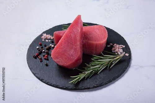 Raw fresh tuna steaks on a black stone board against a light marble background. Side view.