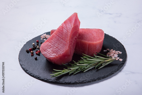 Raw fresh tuna steaks on a black stone board against a light marble background. Side view.