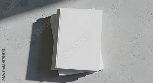Stacked blank white paper, illuminated by natural light creating long shadows on a textured gray wall, a clean and versatile minimalist canvas for creative design and branding content