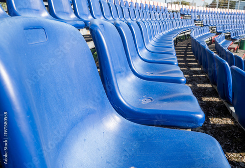 Schilderij op canvas Close perspective of vacant blue plastic chairs arranged in long curved rows across tiered outdoor stadium grandstand creates repetitive geometric pattern under bright natural light
