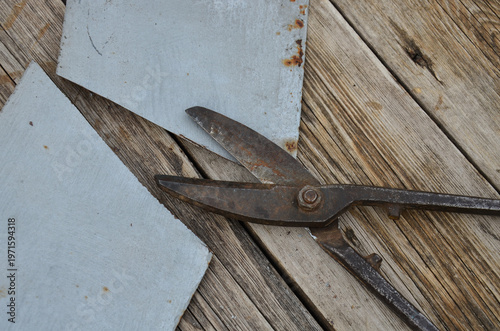 Old rusty metal snips and a cut sheet of metal on a weathered wooden table. Antique metal cutting shears and sliced steel sheet on workshop bench.