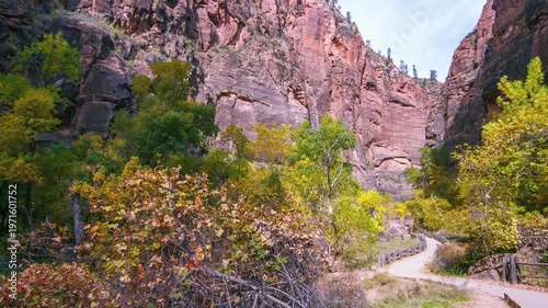 Footage of the scenic and easy Riverside Walk trail in Zion National Park during the fall season. The paved path follows the Virgin River, leading to the start of the famous Narrows hike, surrounded b