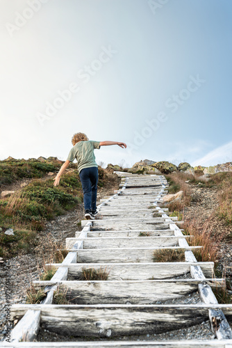 Child playing and balancing on a long wooden staircase in the mountains. Young boy exploring nature and testing his balance during a summer family adventure in scandinavia. authentic lifestyle.
