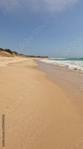 Vertical view first-person walking on the seashore golden sand of a paradisiacal beach with blue sky and turquoise water, in Bolonia Beach, Cadiz, Andalusia, Spain. Point Of View (POV), subjective vie