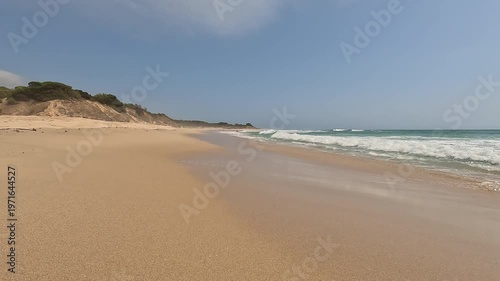 Wild paradise beach with golden sand and turquoise water, gentle waves breaking on the sea shore and blue sky. Bolonia Beach, Cadiz, Andalusia, Spain