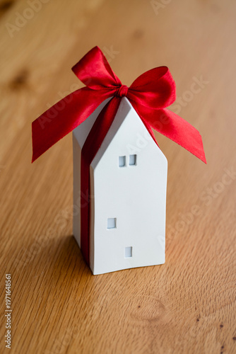 Gift box shaped like a house with a red ribbon sits on a wooden table