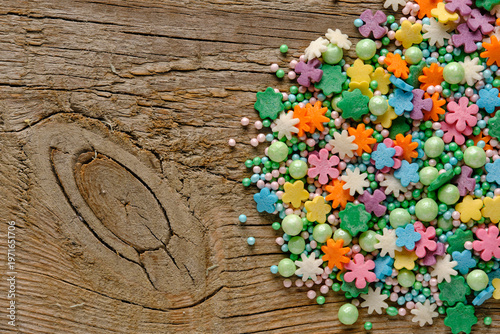 Photos Decorative flower shaped sugar sprinkles and green pearls on an old wooden table, spring baking concept