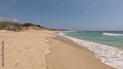 First-person view walking on the seashore golden sand of a paradisiacal beach with blue sky and turquoise water, in Bolonia Beach, Cadiz, Andalusia, Spain. Point Of View (POV), subjective view