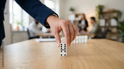 Close up hand pushing domino on wooden table in office meeting with blurred colleagues