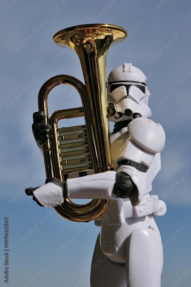 Fototapeta premium Action figure of Star Wars clone trooper in white helmet and armor ready to play on a model of some kind of euphonium brass instrument, blue spring skies with overcast clouds in background. 
