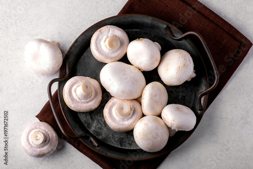 Top view of fresh champignon mushrooms placed in a iron pan resting on a brown linen napkin. The vibrant white mushrooms create a natural and earthy culinary display.