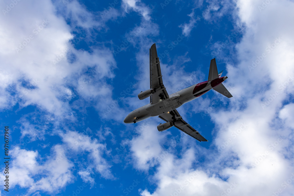 Fototapeta premium Airplane flying through a partly cloudy blue sky, showcasing the underside of the aircraft with visible engines and wings during daytime travel