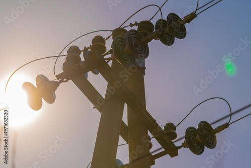 Billede på lærred Backlit pole silhouette with electric lines, low sun creating bright flare and c