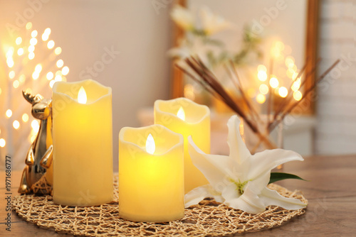 Photos Beautiful LED candles and lily flower on wooden table against blurred lights ind