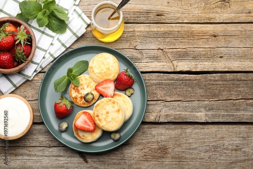 Foto Delicious cottage cheese pancakes with berries, mint, sour cream and honey on wooden table, flat lay