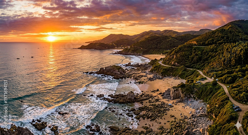 A magnificent aerial view reveals a rugged coastline bathed in the golden light of sunset, with powerful waves crashing against rocks, a sandy beach, and a scenic winding road.