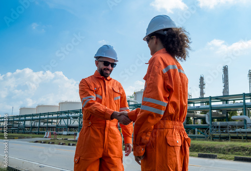 Professional male female engineer  jumpsuit shak hand front oil refinery infrastructure representing successful business partnership industrial agreement teamwork corporate achievement energy sector