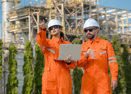 professional female industrial engineer jumpsuit point toward refinery plant  male colleague hold laptop chemical flask representing visionary leadership oil gas quality inspection teamwork energy