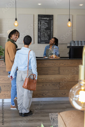 Diverse customers with African American barista ordering drinks at coffee counter with pastry dome