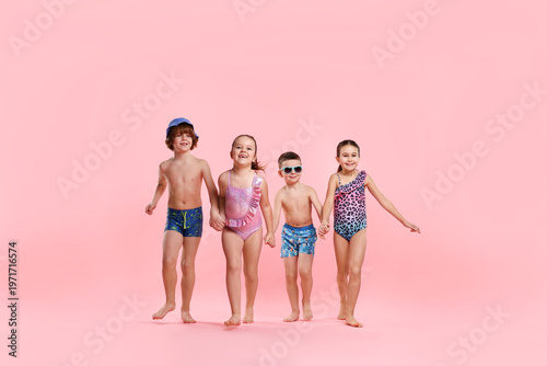 Bild auf Leinwand Children in swimwear with beach accessories walking on pink background