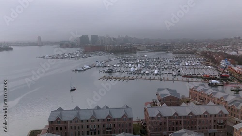 The Canton Waterfront in downtown Baltimore with boats in view, apartments near by and buildings in foggy horizon.