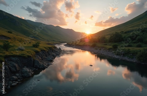 River flows between green hills at sunset. Sun rays reflect in calm water surface. Clouds float in warm orange sky over landscape. Natural beauty shines bright.