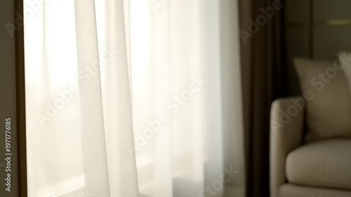 A serene living room scene with a beige armchair next to a window with sheer curtains letting in natural light indoors.