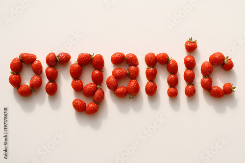 Strawberries are carefully arranged to spell organic on a smooth white surface with bright lighting creating a fresh vibrant look and highlighting the natural red color