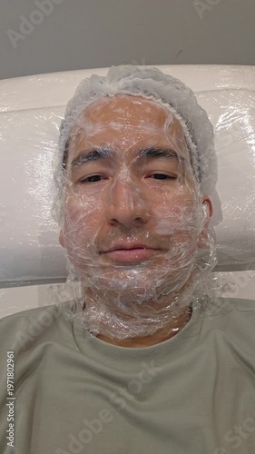 Treatment, cure of face skin in dermatology clinic. Scars procedure with problem skin for man. Man with cream with anesthesia and plastic film on his face before laser therapy procedure.