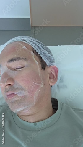Facial mask of man in dermatologist office. Man on with therapy room. Man lying on bed. Healing clay to relieve laser treatment. Close-up of a man's face. Vertical.